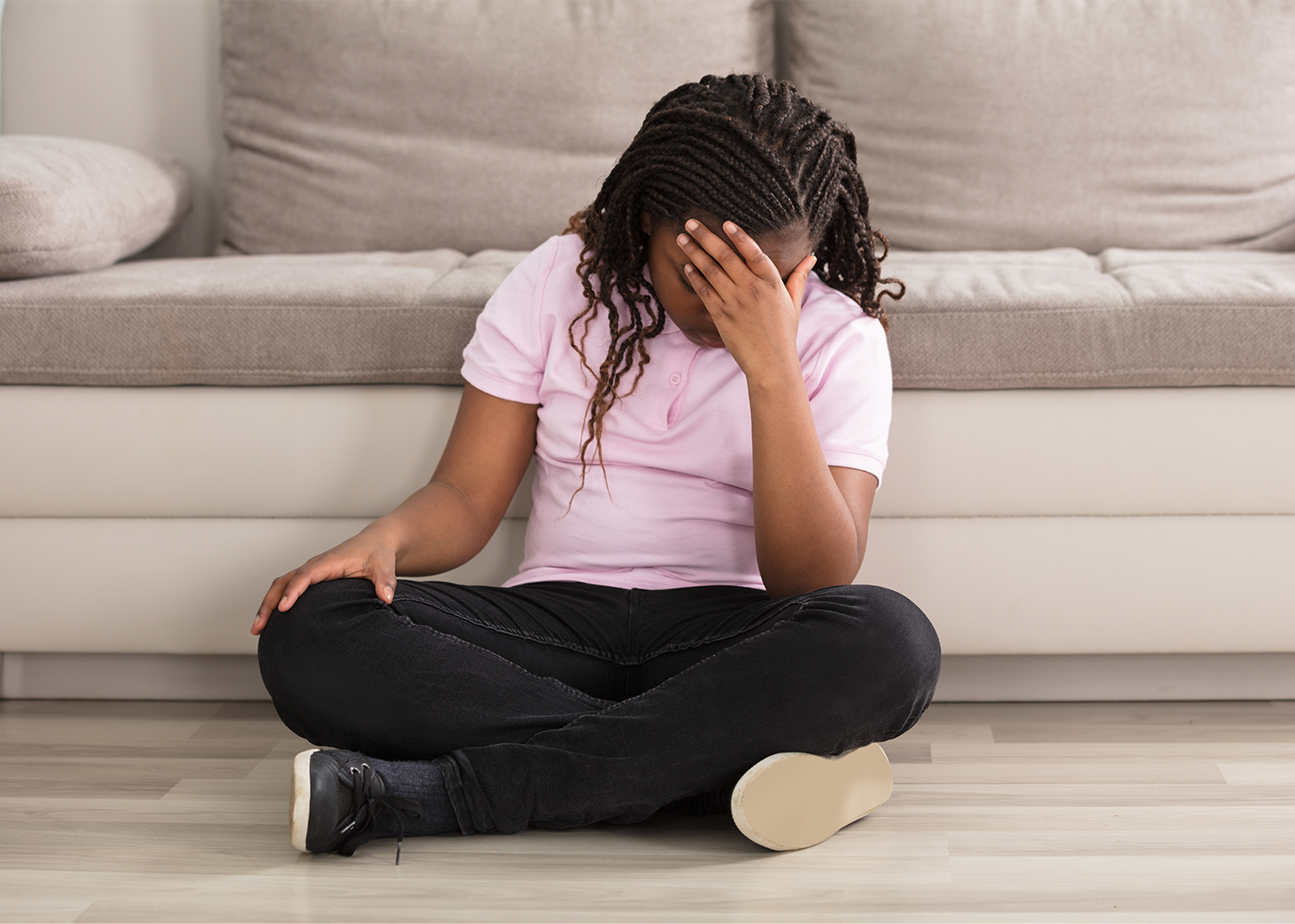Teenage girl sitting on the floor with her hand over her face appearing stressed.