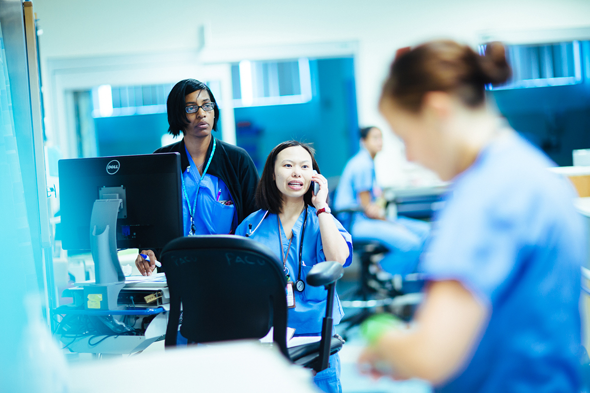 A provider speaks on a cell phone in the midst of the Emergency department while other colleagues look on